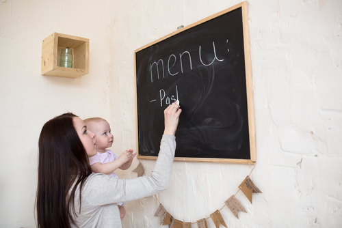 Mãe escrevendo cardápio nutricional com bebê no colo